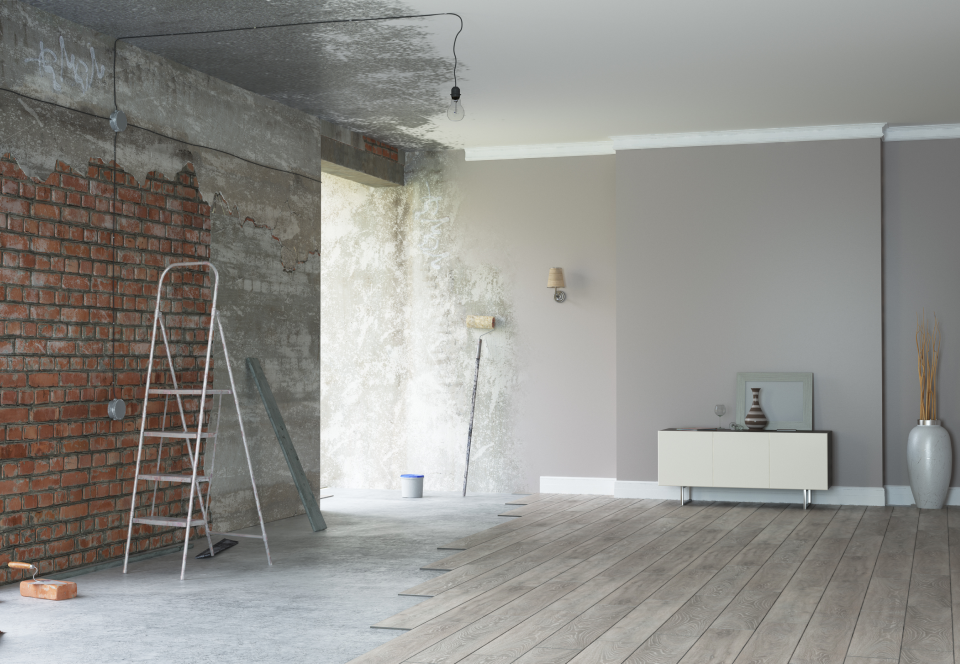 Ein unfertiger Raum mit freiliegenden Ziegel- und Betonwänden, einer Leiter und Malermaterialien, der die laufenden Renovierungsarbeiten zeigt.