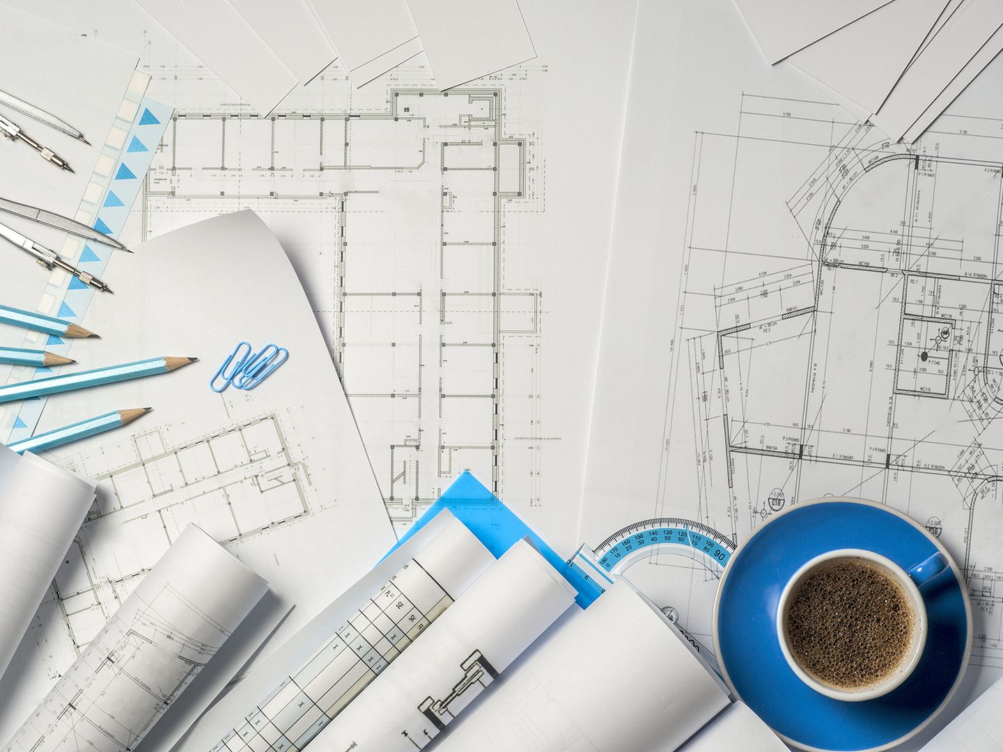 Eine Sammlung von architektonischen Entwürfen, Bleistiften, Büroklammern und einer Tasse Kaffee auf einem Schreibtisch, die den Entwurfsprozess veranschaulicht.